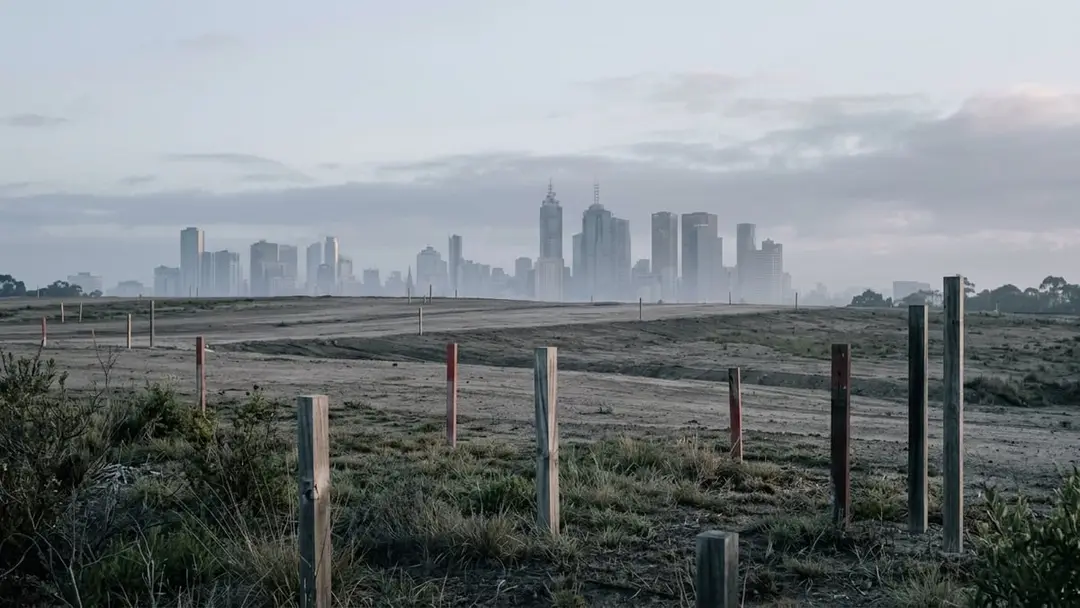 Cleared development site with timber survey pegs and distant city towers in haze