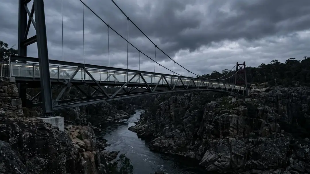 Steel and glass footbridge spanning a dark gorge under a stormy sky